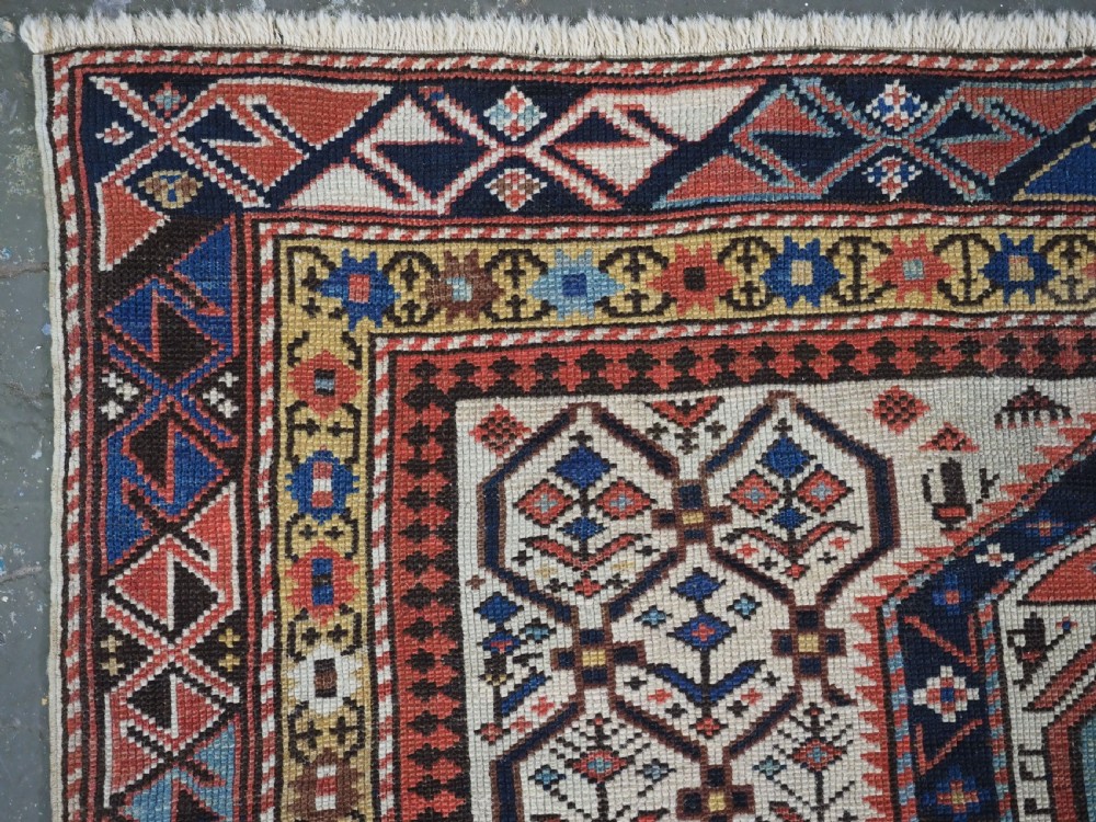 An antique Caucasian Shirvan wool prayer rug featuring an ivory field covered in a geometric floral lattice motif, enclosed by a multi-bordered frame and a stepped prayer arch at the top. View V