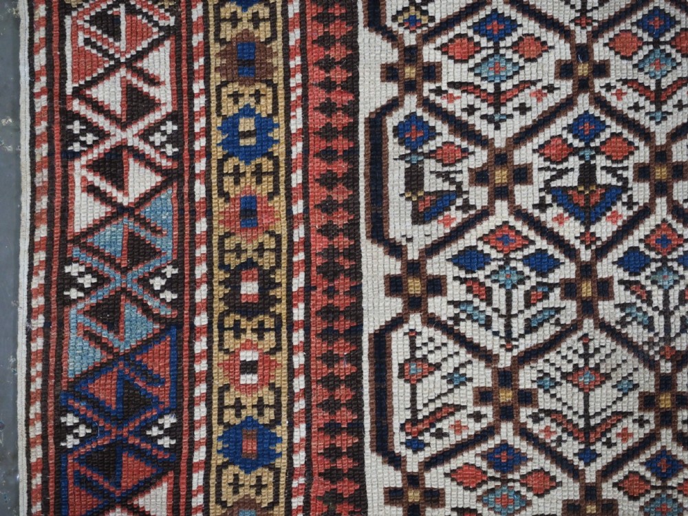 An antique Caucasian Shirvan wool prayer rug featuring an ivory field covered in a geometric floral lattice motif, enclosed by a multi-bordered frame and a stepped prayer arch at the top. View VI