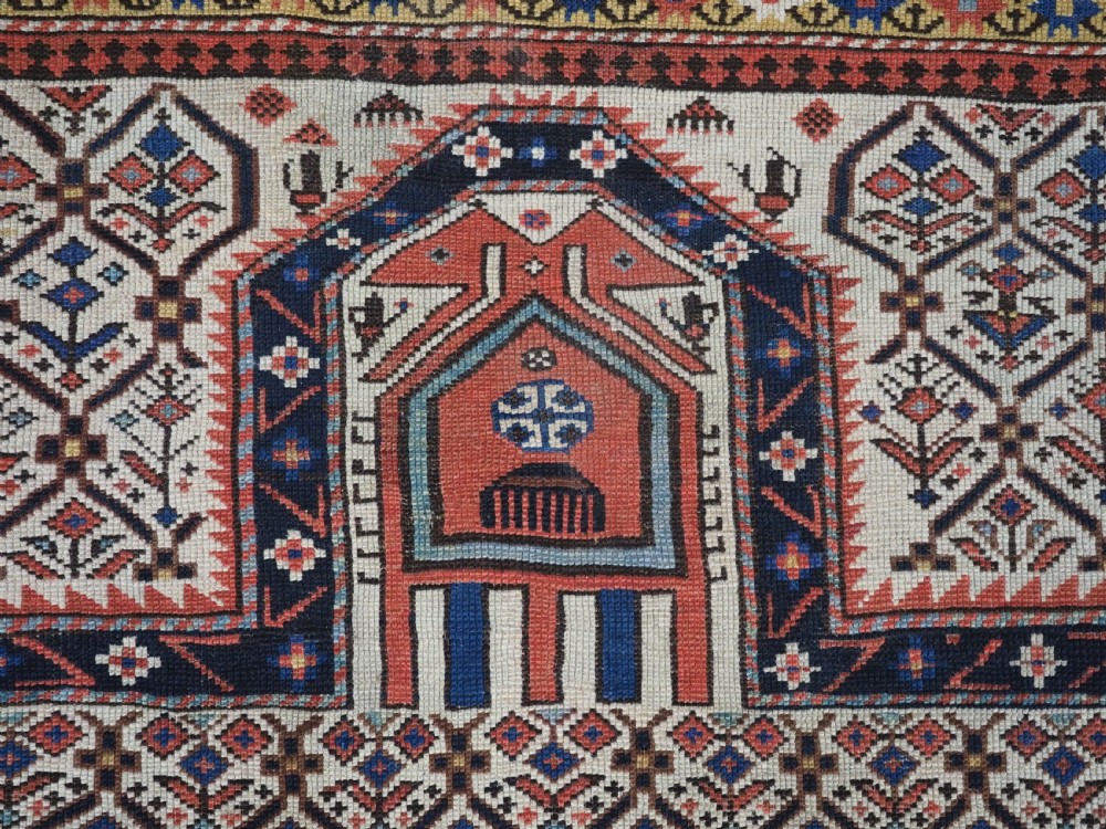 An antique Caucasian Shirvan wool prayer rug featuring an ivory field covered in a geometric floral lattice motif, enclosed by a multi-bordered frame and a stepped prayer arch at the top. View VII