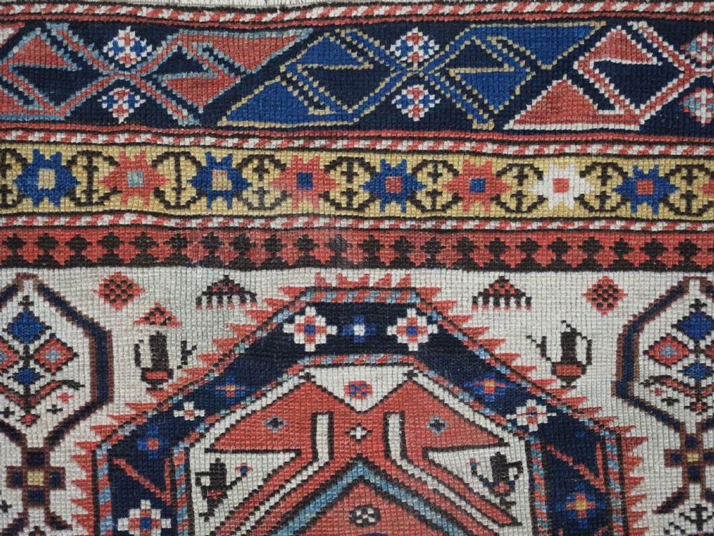 An antique Caucasian Shirvan wool prayer rug featuring an ivory field covered in a geometric floral lattice motif, enclosed by a multi-bordered frame and a stepped prayer arch at the top. View IX