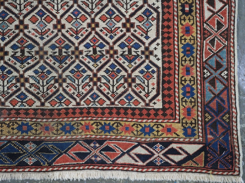 An antique Caucasian Shirvan wool prayer rug featuring an ivory field covered in a geometric floral lattice motif, enclosed by a multi-bordered frame and a stepped prayer arch at the top. View XII