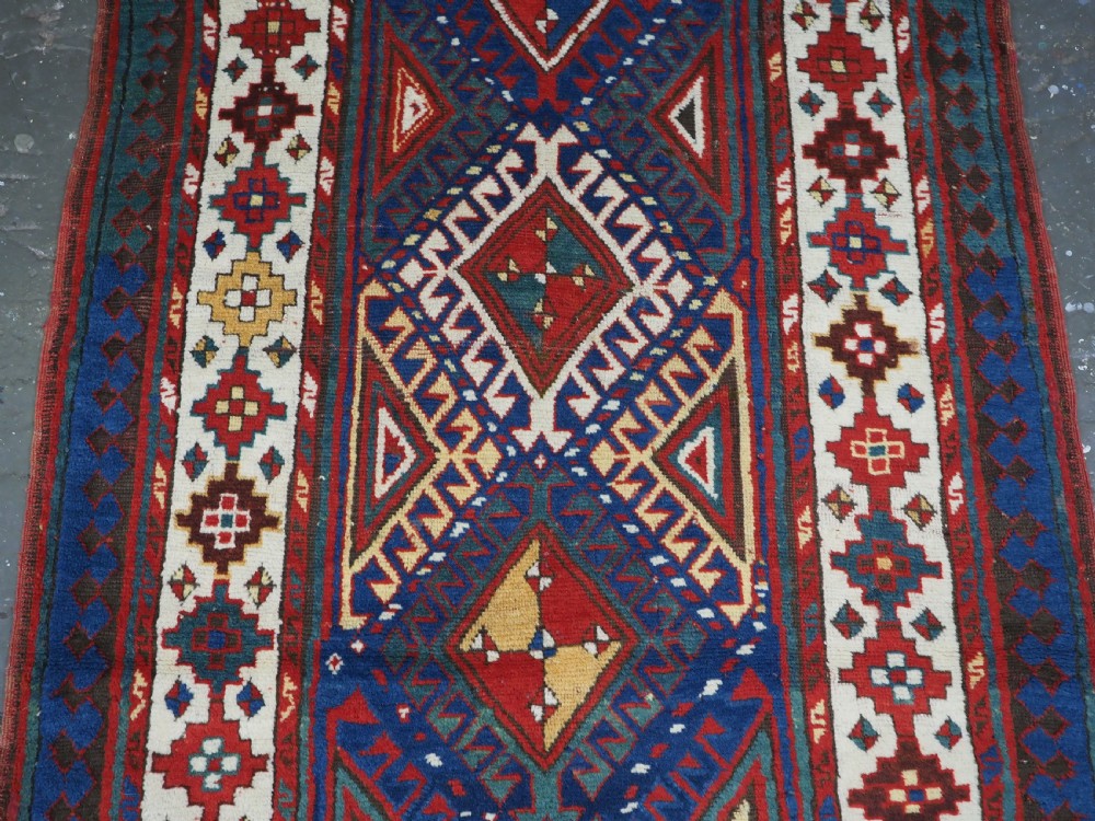 An antique Caucasian Moghan Kazak wool runner rug with repeating diamond hooked medallions on a deep blue field and geometric borders. View III