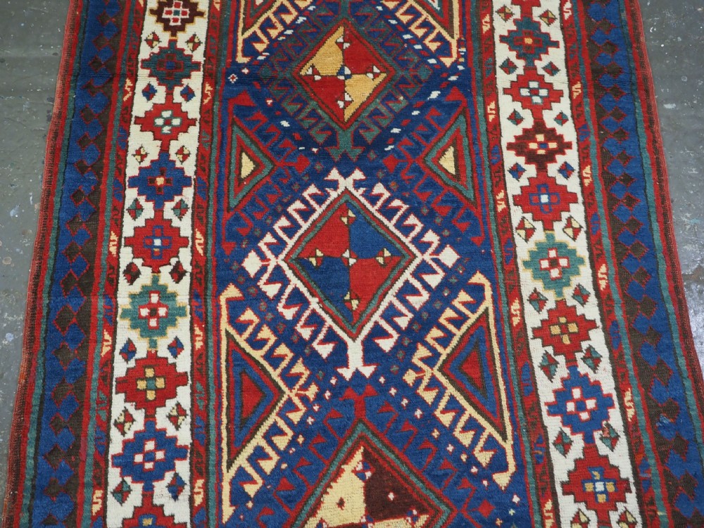 An antique Caucasian Moghan Kazak wool runner rug with repeating diamond hooked medallions on a deep blue field and geometric borders. View IV