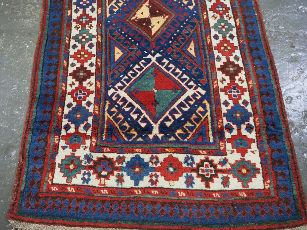 An antique Caucasian Moghan Kazak wool runner rug with repeating diamond hooked medallions on a deep blue field and geometric borders. View V