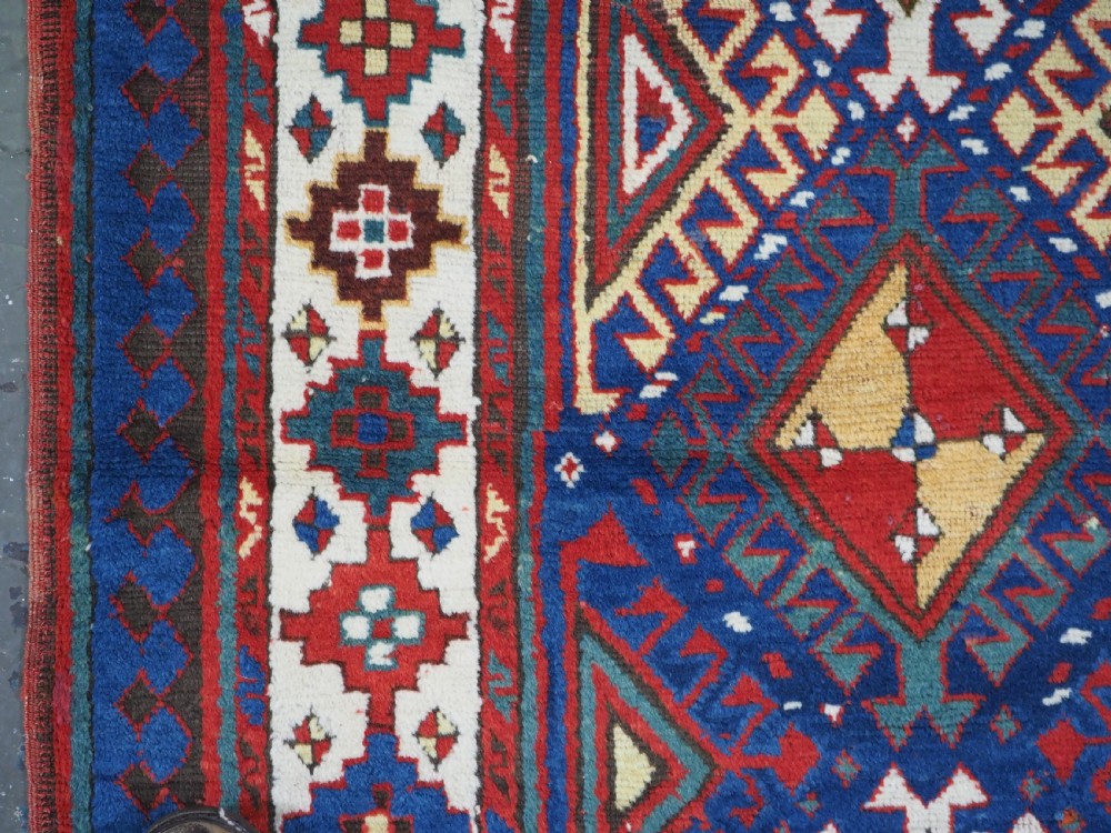 An antique Caucasian Moghan Kazak wool runner rug with repeating diamond hooked medallions on a deep blue field and geometric borders. View VII