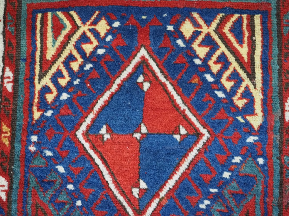 An antique Caucasian Moghan Kazak wool runner rug with repeating diamond hooked medallions on a deep blue field and geometric borders. View VIII