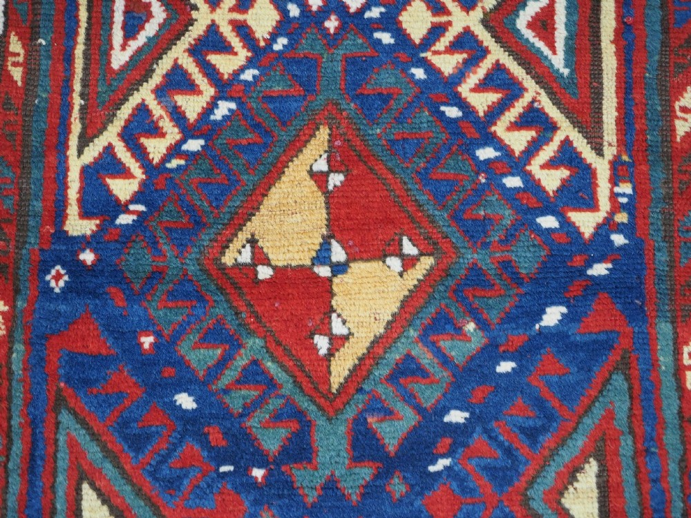 An antique Caucasian Moghan Kazak wool runner rug with repeating diamond hooked medallions on a deep blue field and geometric borders. View IX