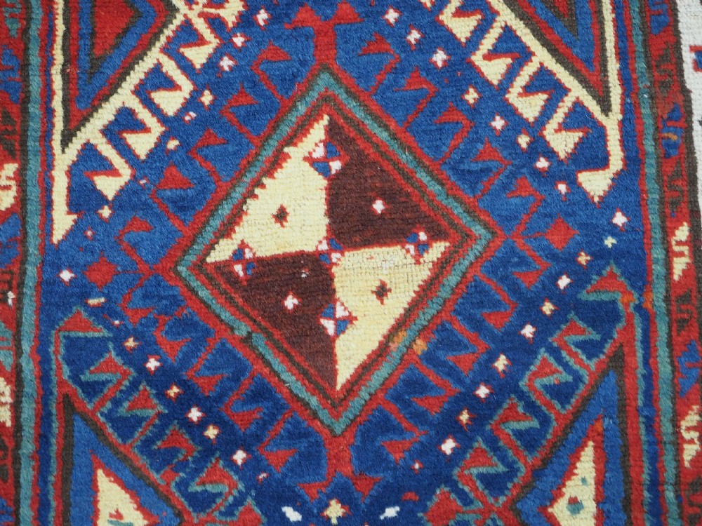 An antique Caucasian Moghan Kazak wool runner rug with repeating diamond hooked medallions on a deep blue field and geometric borders. View X