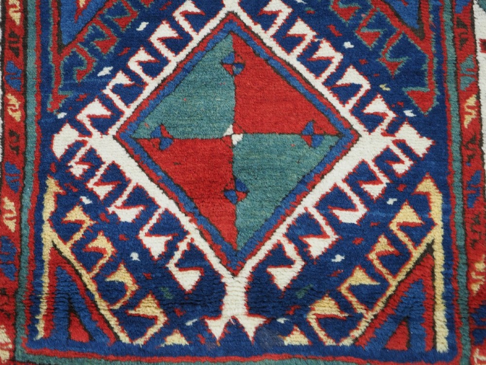 An antique Caucasian Moghan Kazak wool runner rug with repeating diamond hooked medallions on a deep blue field and geometric borders. View XI