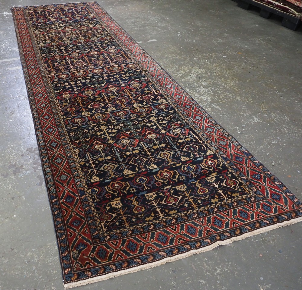 An antique handwoven wool Caucasian Kuba runner featuring dense geometric motifs in red, blue, and cream shades across a long dark navy field. View II