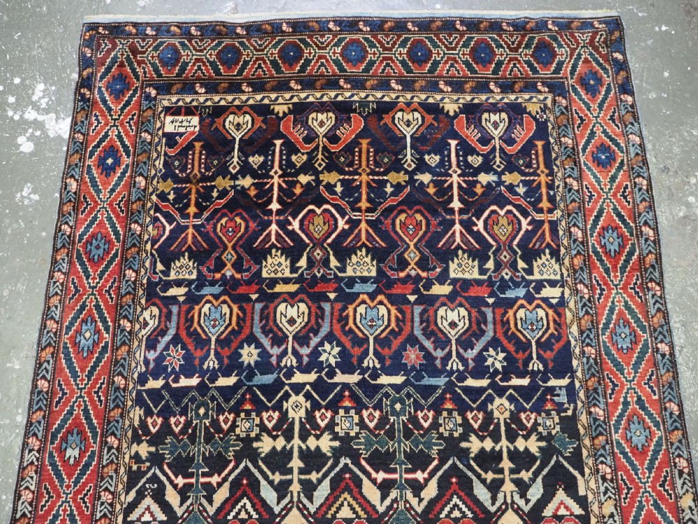 An antique handwoven wool Caucasian Kuba runner featuring dense geometric motifs in red, blue, and cream shades across a long dark navy field. View III