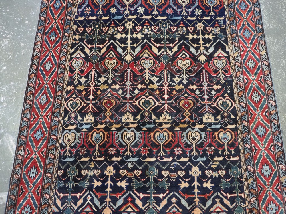 An antique handwoven wool Caucasian Kuba runner featuring dense geometric motifs in red, blue, and cream shades across a long dark navy field. View V