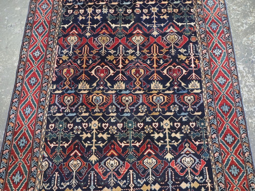 An antique handwoven wool Caucasian Kuba runner featuring dense geometric motifs in red, blue, and cream shades across a long dark navy field. View VI