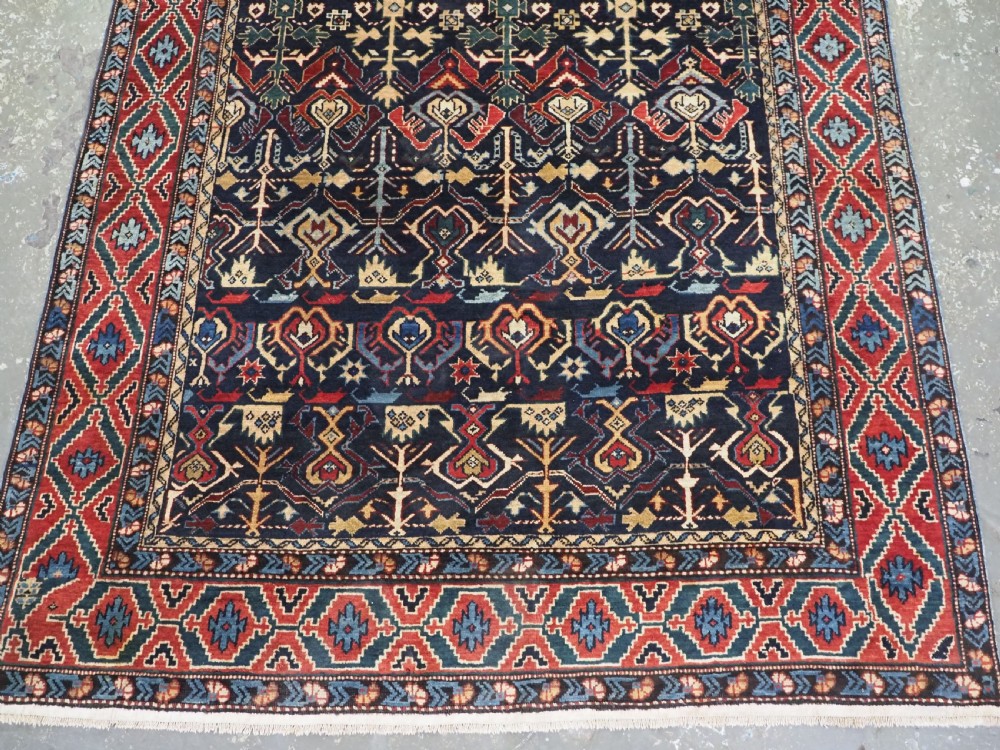 An antique handwoven wool Caucasian Kuba runner featuring dense geometric motifs in red, blue, and cream shades across a long dark navy field. View VII