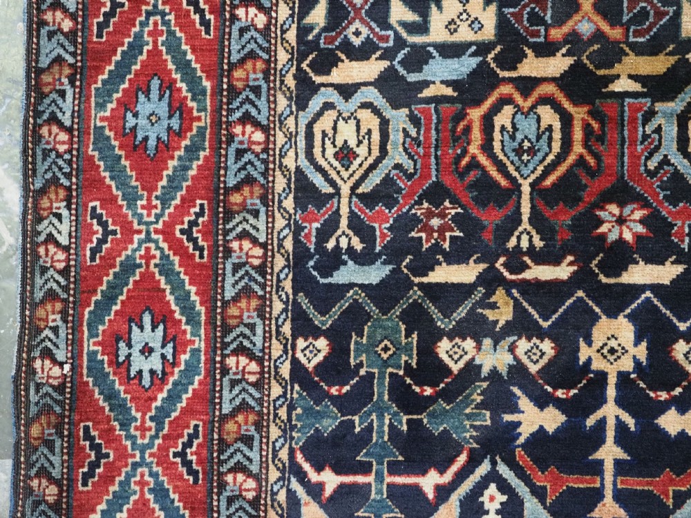 An antique handwoven wool Caucasian Kuba runner featuring dense geometric motifs in red, blue, and cream shades across a long dark navy field. View IX