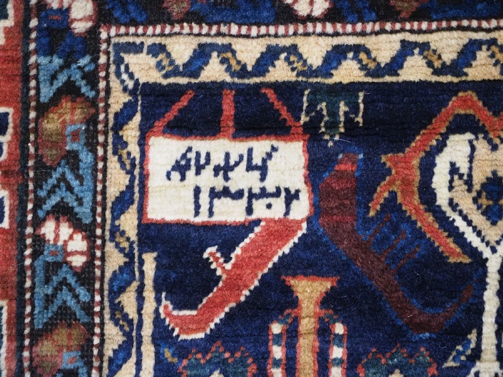 An antique handwoven wool Caucasian Kuba runner featuring dense geometric motifs in red, blue, and cream shades across a long dark navy field. View X