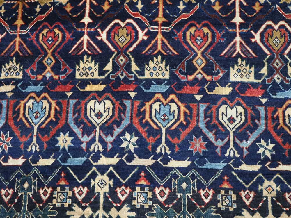 An antique handwoven wool Caucasian Kuba runner featuring dense geometric motifs in red, blue, and cream shades across a long dark navy field. View XI
