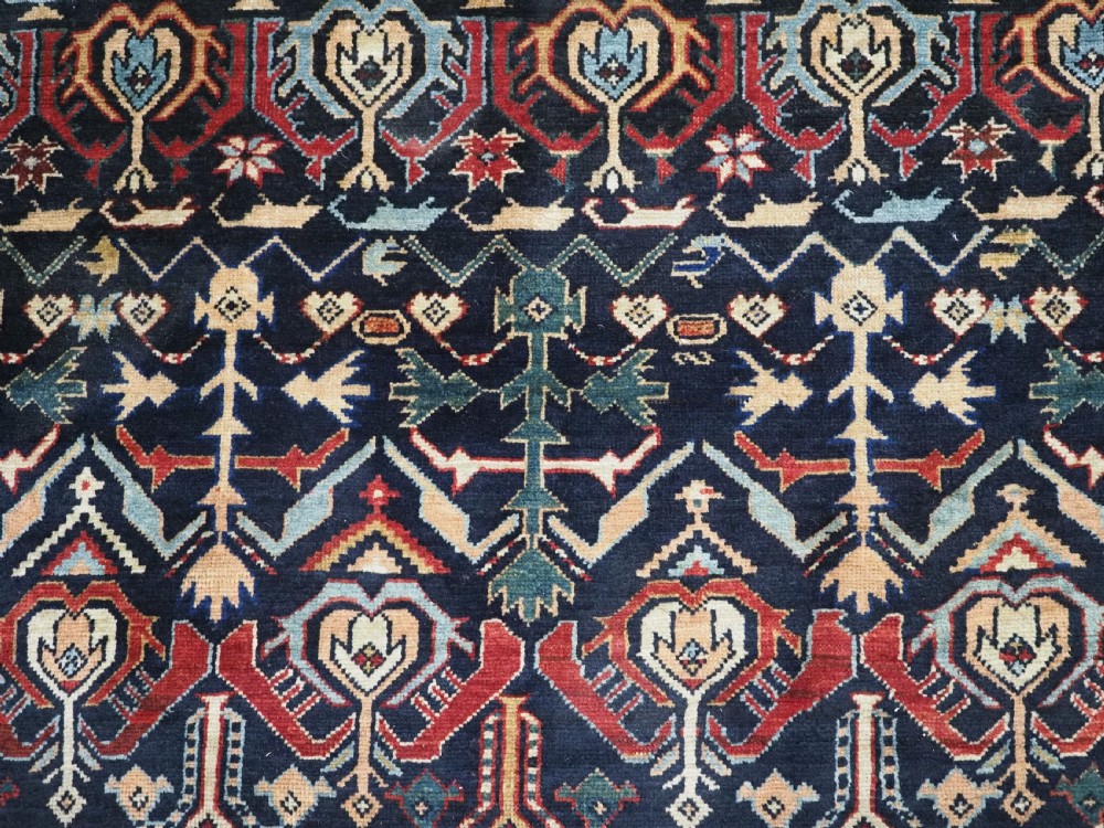 An antique handwoven wool Caucasian Kuba runner featuring dense geometric motifs in red, blue, and cream shades across a long dark navy field. View XII