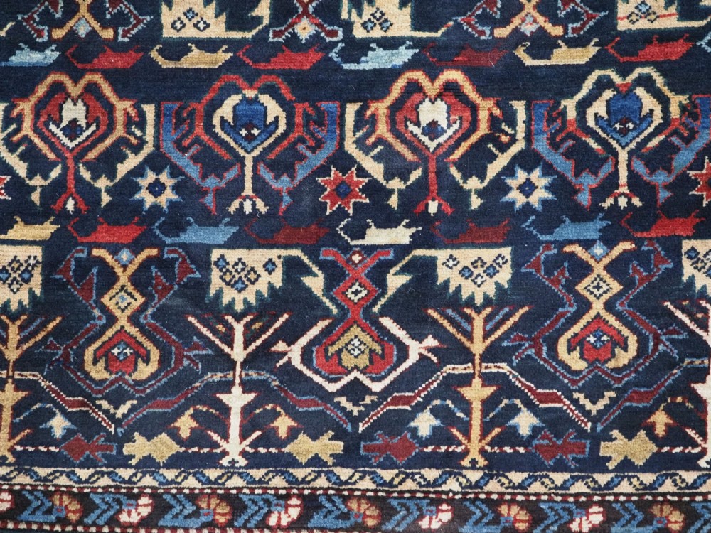 An antique handwoven wool Caucasian Kuba runner featuring dense geometric motifs in red, blue, and cream shades across a long dark navy field. View XIV