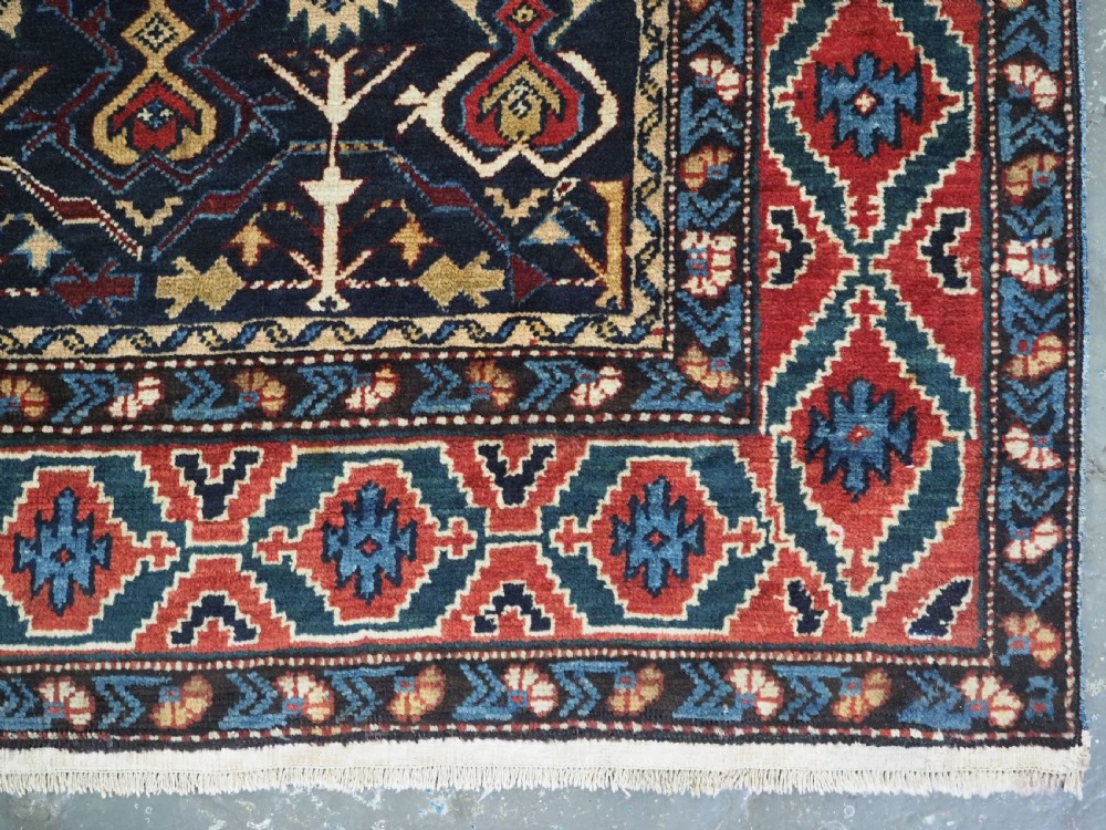 An antique handwoven wool Caucasian Kuba runner featuring dense geometric motifs in red, blue, and cream shades across a long dark navy field. View XV