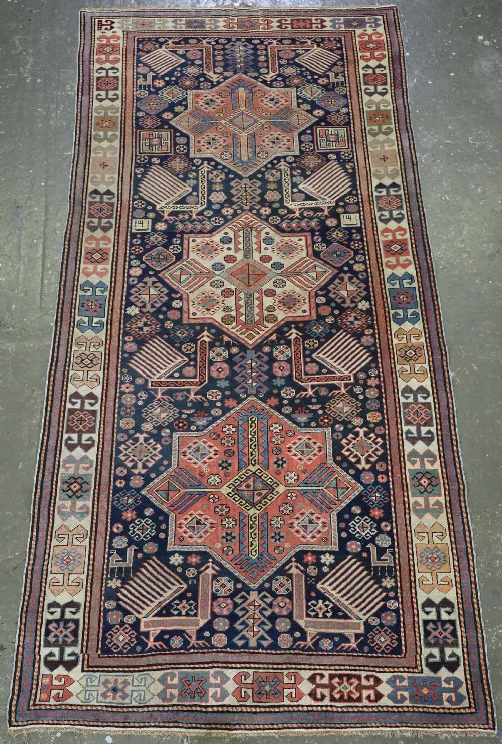 An antique Caucasian Akstafa long rug runner featuring three star medallions and stylized peacock motifs on a dark navy blue field with geometric borders.