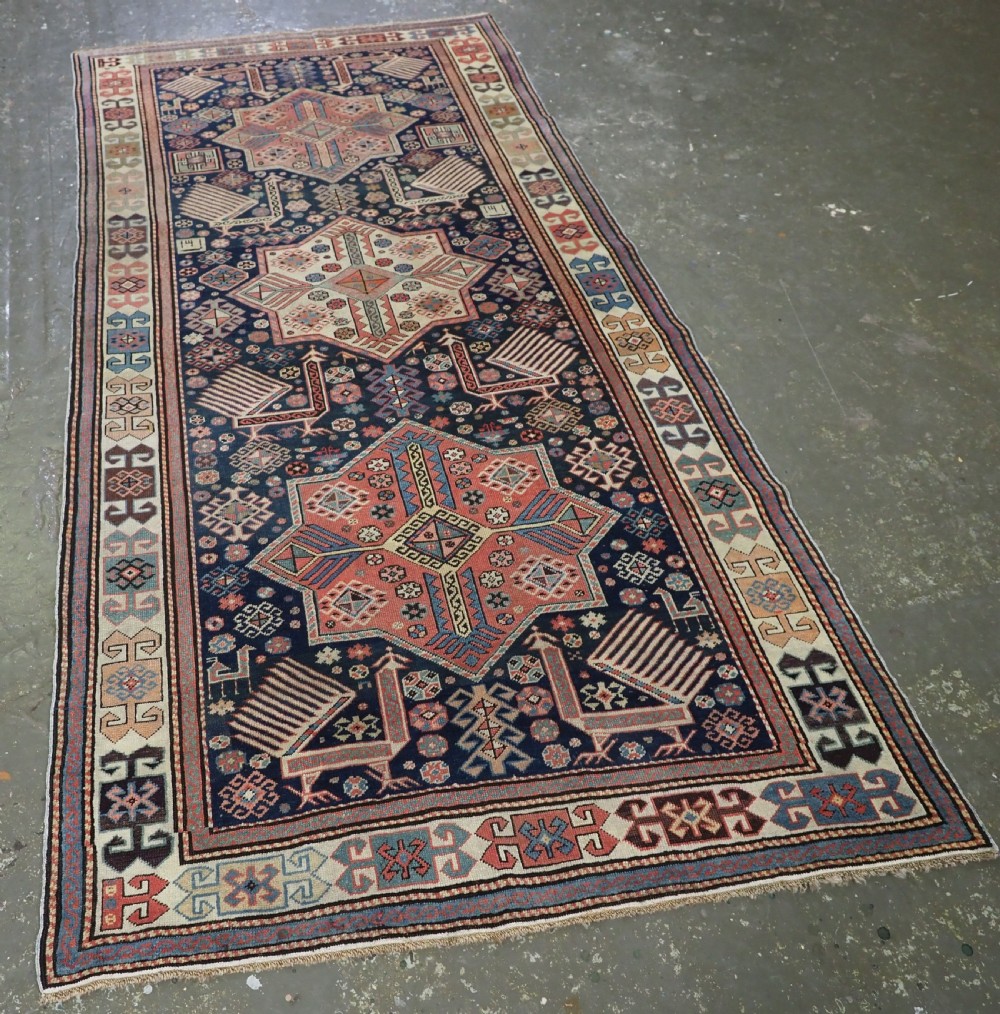 An antique Caucasian Akstafa long rug runner featuring three star medallions and stylized peacock motifs on a dark navy blue field with geometric borders. View II