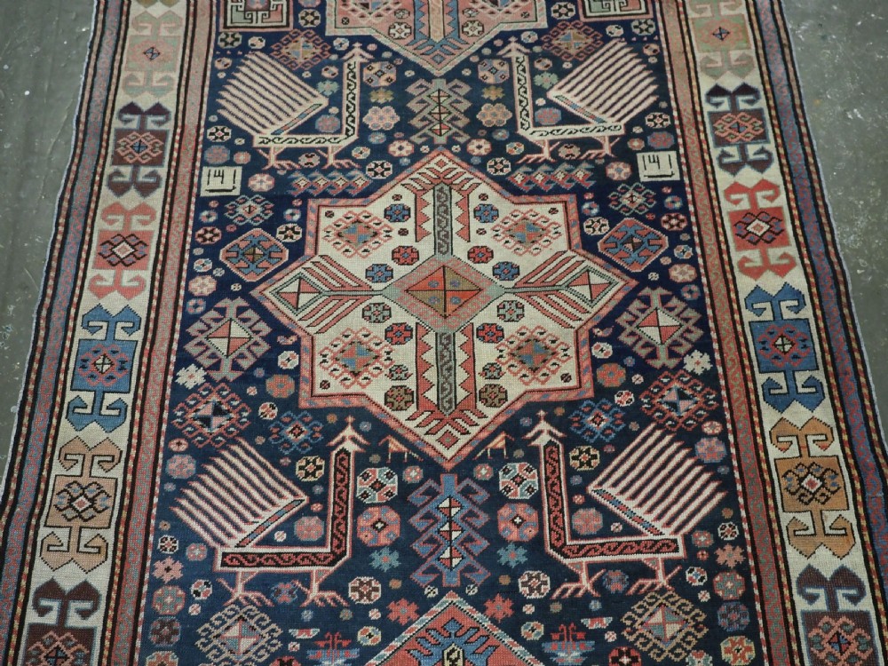 An antique Caucasian Akstafa long rug runner featuring three star medallions and stylized peacock motifs on a dark navy blue field with geometric borders. View IV