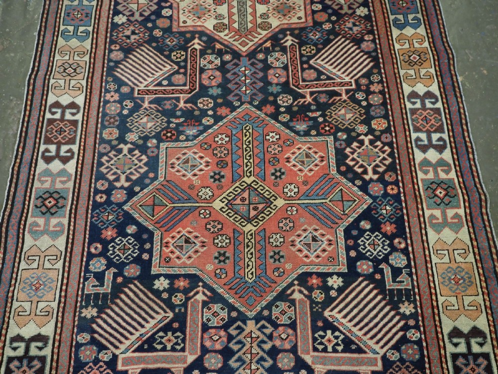 An antique Caucasian Akstafa long rug runner featuring three star medallions and stylized peacock motifs on a dark navy blue field with geometric borders. View V