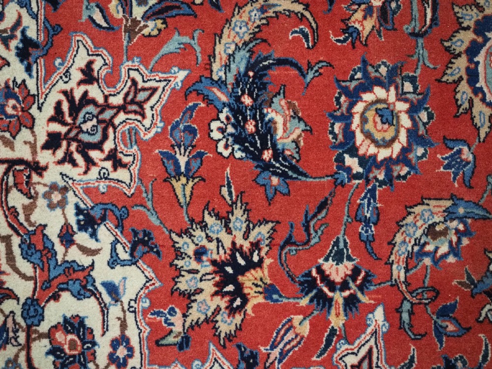 An antique Persian Isfahan carpet featuring a detailed red central field with floral motifs, framed by light spandrels and a wide blue floral border. View XII