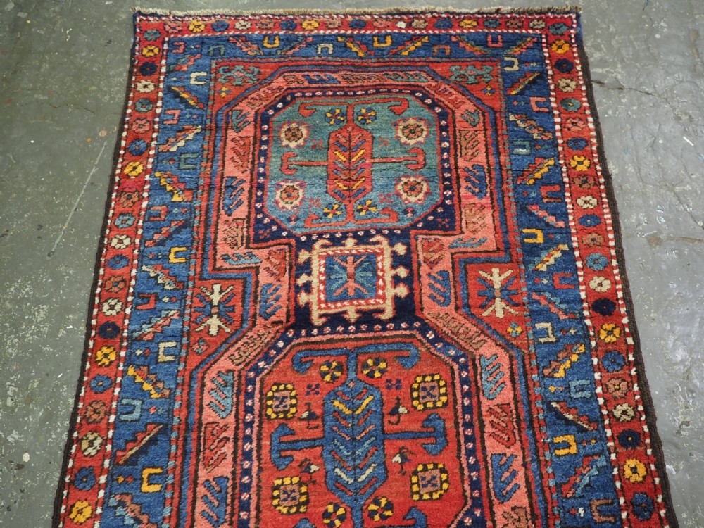 A long hand-knotted wool runner rug featuring geometric garden medallions in indigo blue, terracotta red, and gold within a patterned border. View IV