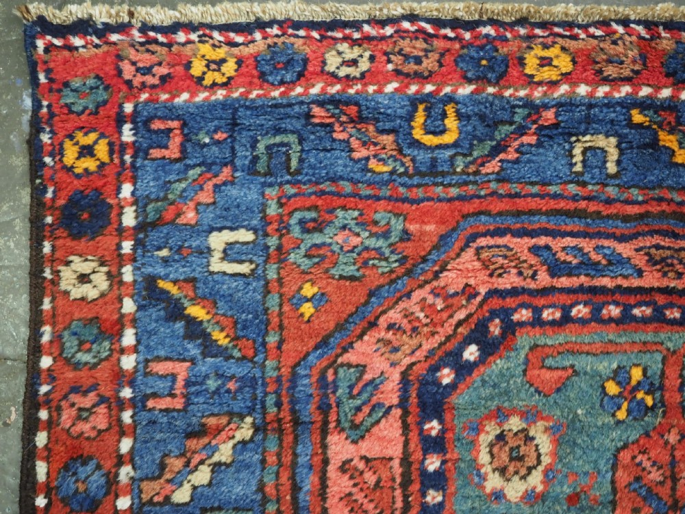 A long hand-knotted wool runner rug featuring geometric garden medallions in indigo blue, terracotta red, and gold within a patterned border. View IX