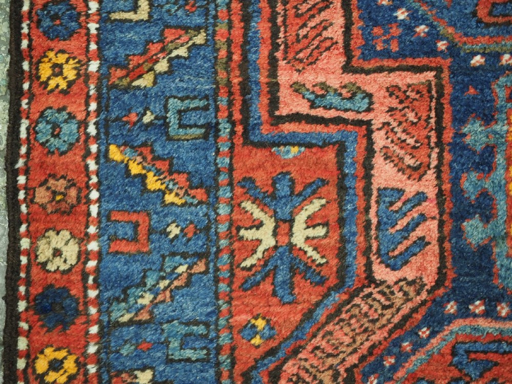 A long hand-knotted wool runner rug featuring geometric garden medallions in indigo blue, terracotta red, and gold within a patterned border. View X