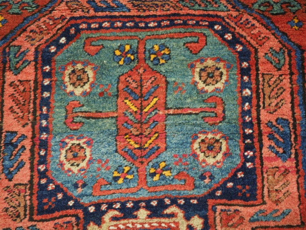 A long hand-knotted wool runner rug featuring geometric garden medallions in indigo blue, terracotta red, and gold within a patterned border. View XI