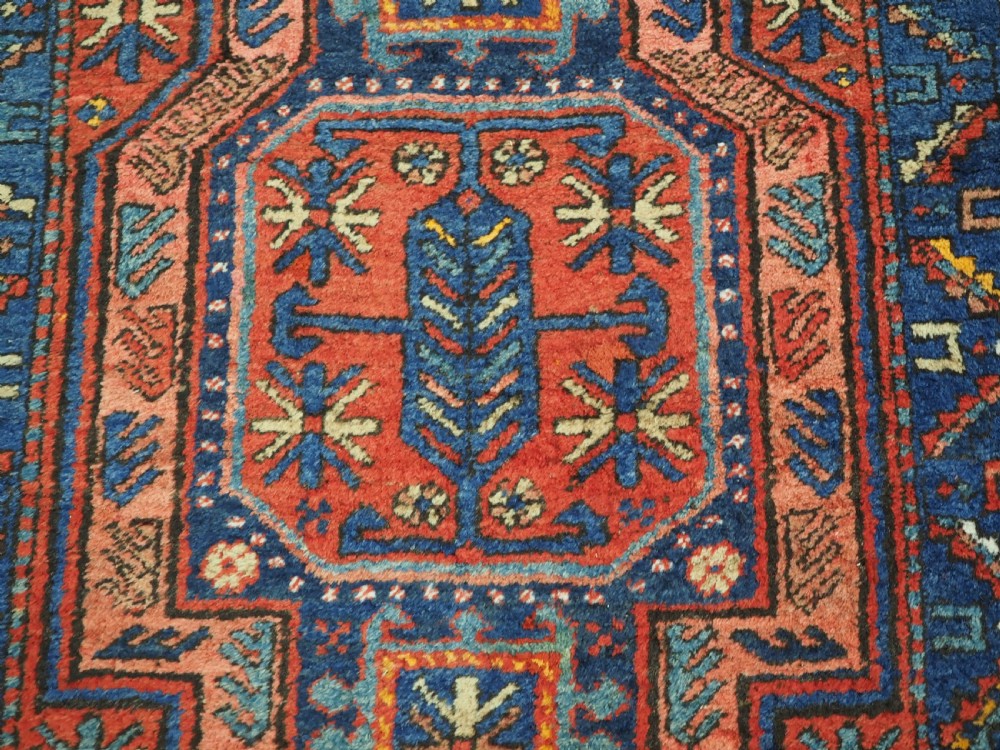 A long hand-knotted wool runner rug featuring geometric garden medallions in indigo blue, terracotta red, and gold within a patterned border. View XII