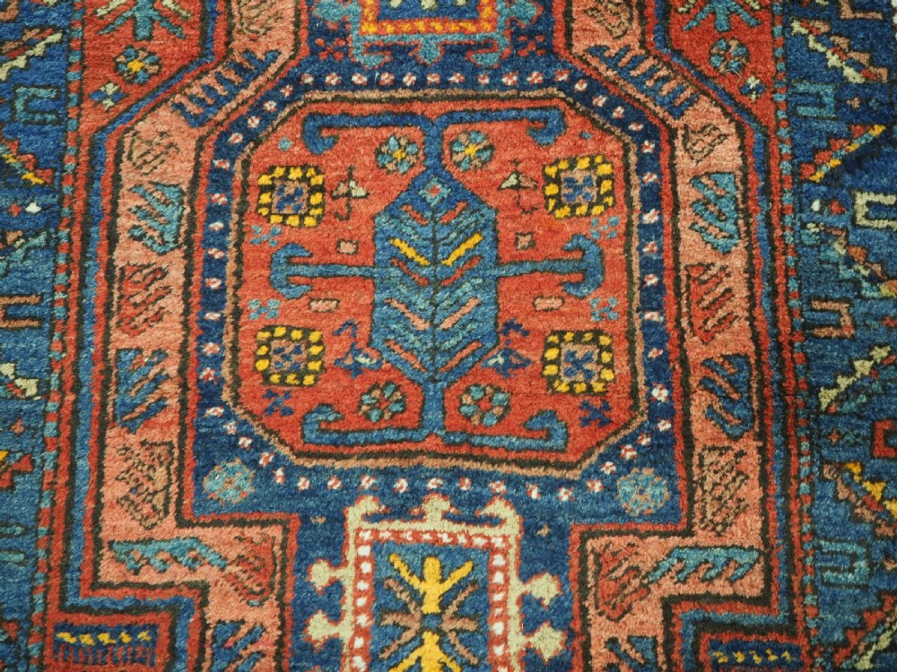 A long hand-knotted wool runner rug featuring geometric garden medallions in indigo blue, terracotta red, and gold within a patterned border. View XIII