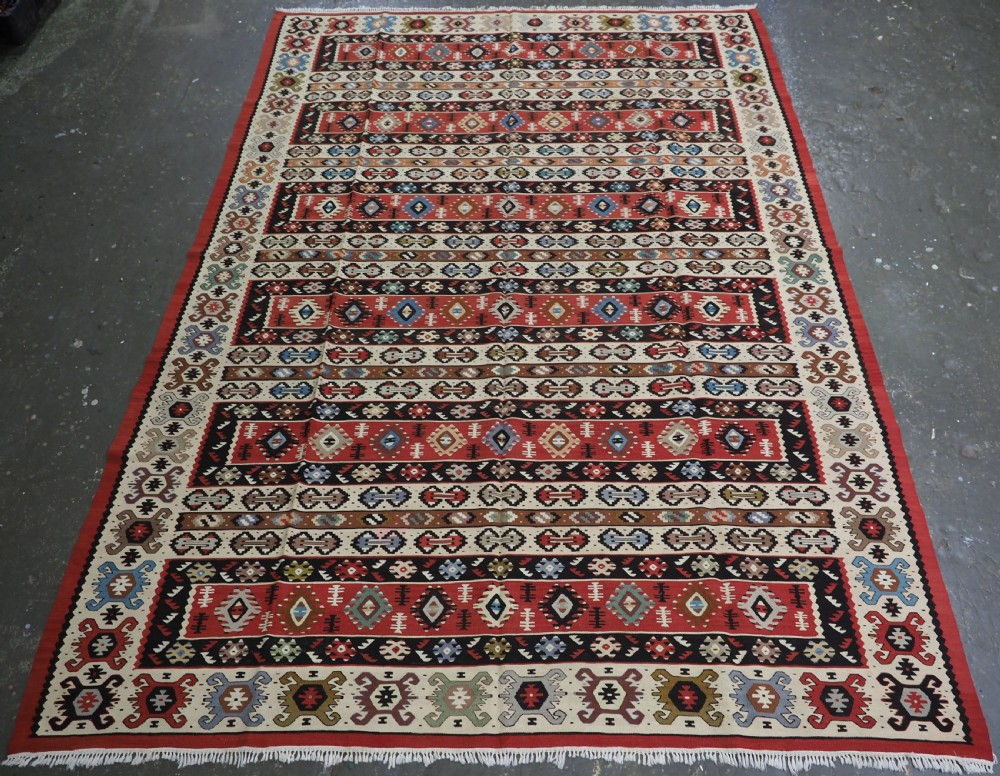 An antique flatweave Pirot Sarkoy wool rug featuring horizontal geometric bands in red, cream, black, and blue.