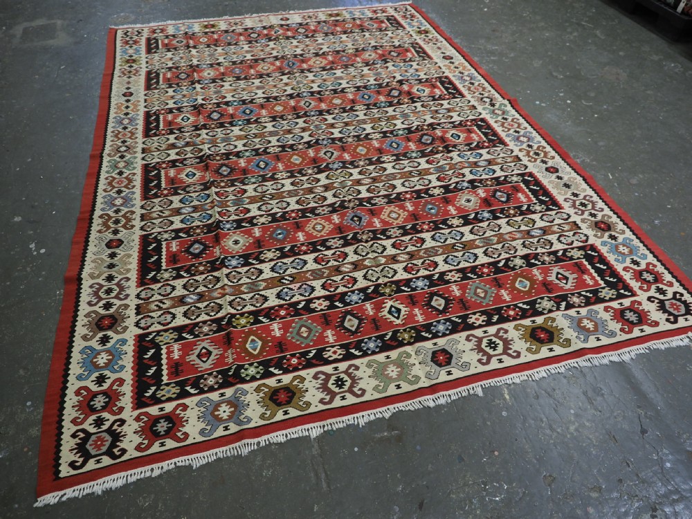 An antique flatweave Pirot Sarkoy wool rug featuring horizontal geometric bands in red, cream, black, and blue. View II