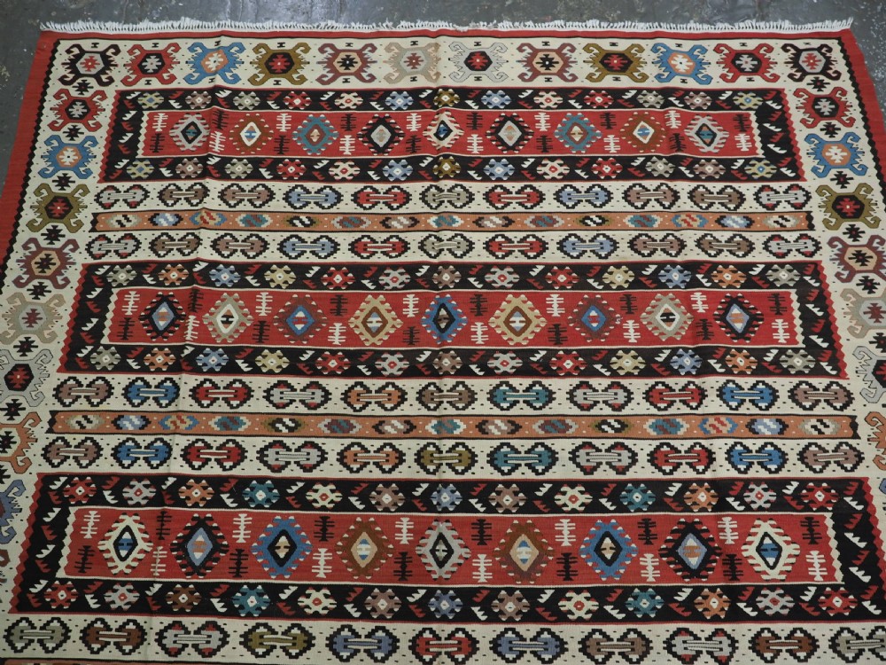 An antique flatweave Pirot Sarkoy wool rug featuring horizontal geometric bands in red, cream, black, and blue. View III