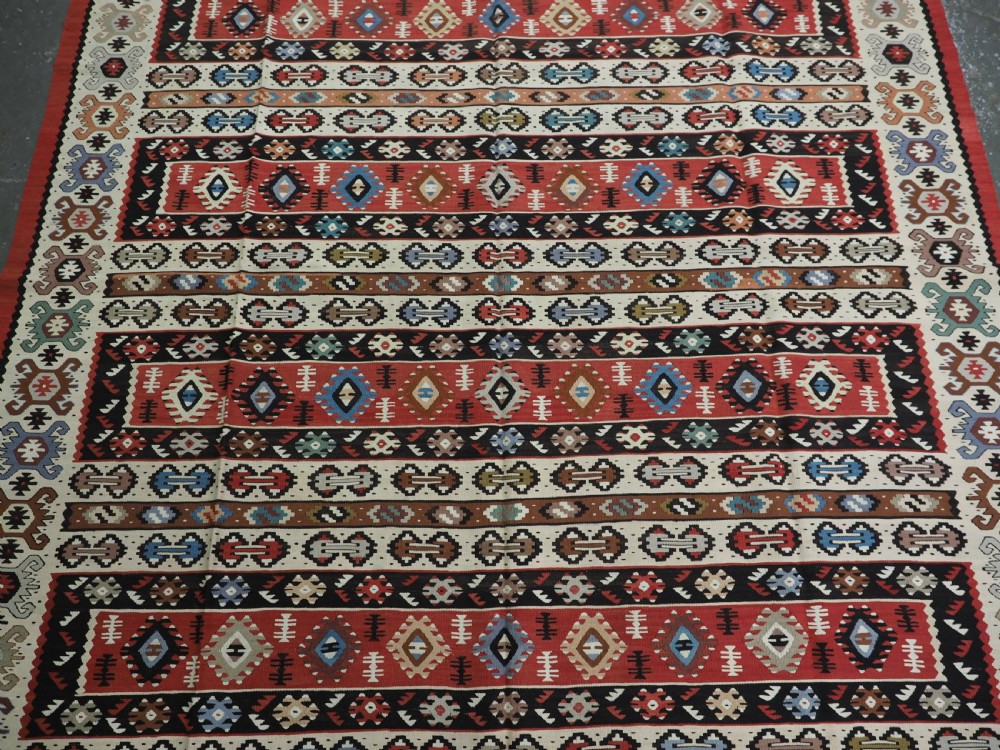 An antique flatweave Pirot Sarkoy wool rug featuring horizontal geometric bands in red, cream, black, and blue. View IV