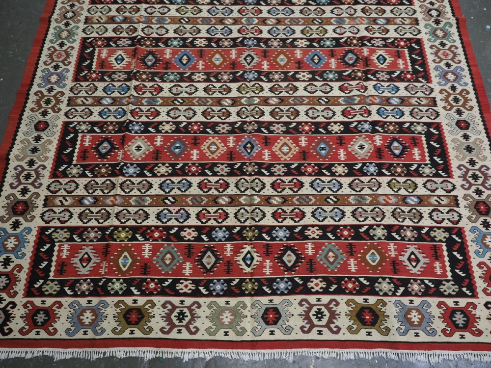 An antique flatweave Pirot Sarkoy wool rug featuring horizontal geometric bands in red, cream, black, and blue. View V