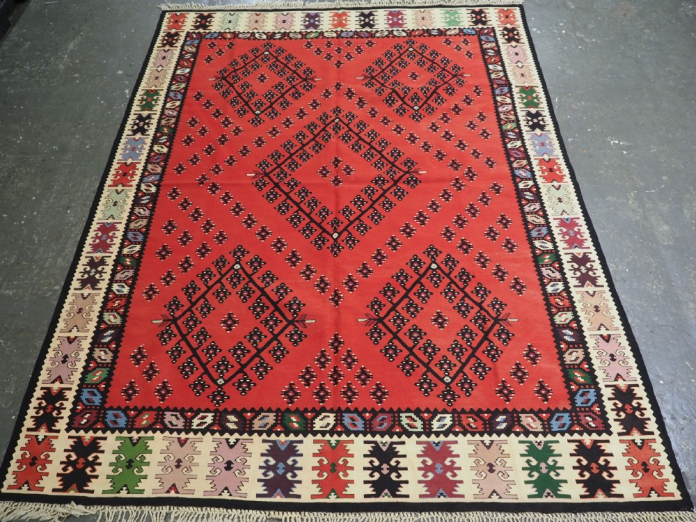 An antique red flat-weave Pirot Sarkoy wool kilim featuring geometric diamond motifs and a multi-coloured decorative border.