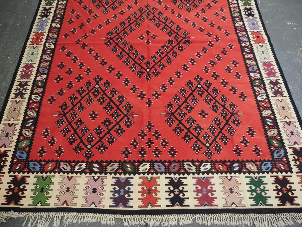 An antique red flat-weave Pirot Sarkoy wool kilim featuring geometric diamond motifs and a multi-coloured decorative border. View V