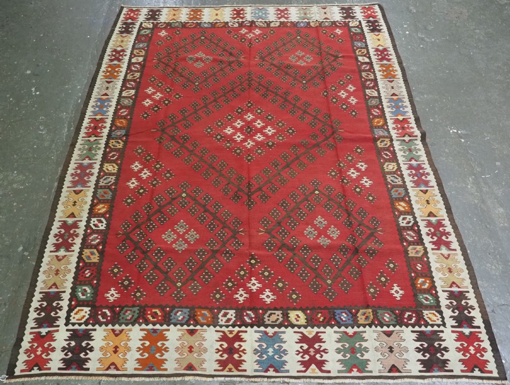 A red flatwoven antique Pirot Sarkoy kilim featuring geometric diamond motifs with intricate multi-coloured borders.