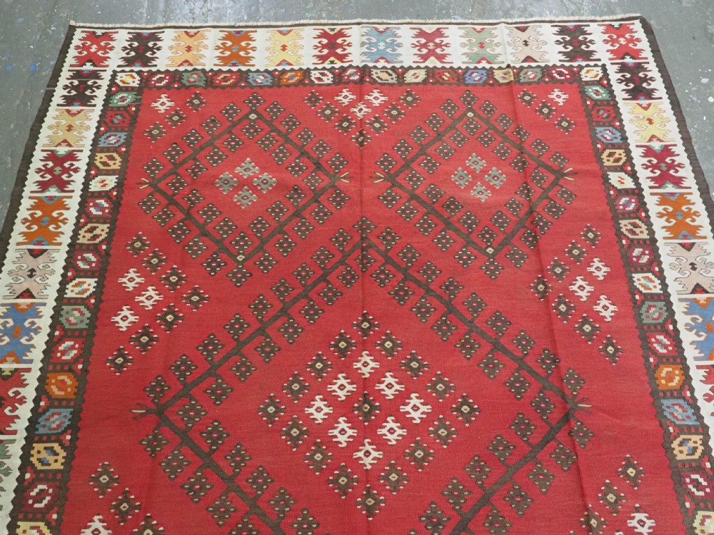 A red flatwoven antique Pirot Sarkoy kilim featuring geometric diamond motifs with intricate multi-coloured borders. View III