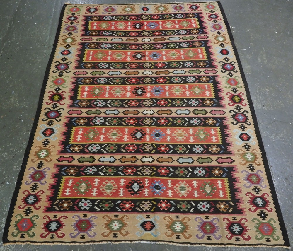 A handwoven antique Pirot Sarkoy flatweave wool kilim rug featuring horizontal bands of geometric motifs in terracotta, beige, yellow, green, and dark brown.