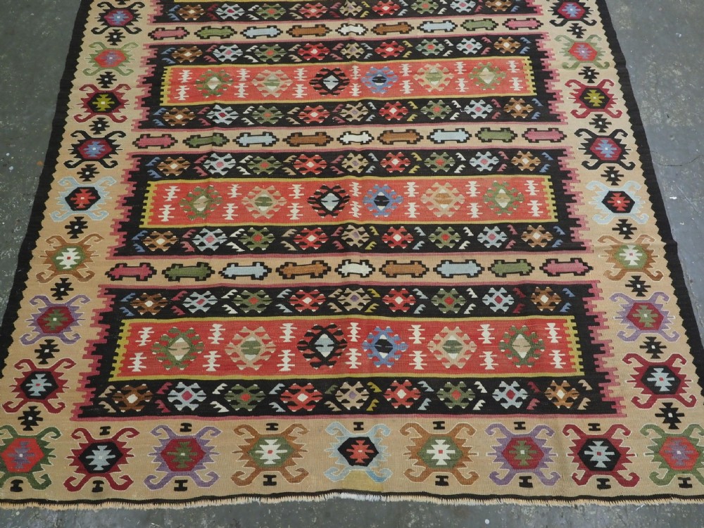 A handwoven antique Pirot Sarkoy flatweave wool kilim rug featuring horizontal bands of geometric motifs in terracotta, beige, yellow, green, and dark brown. View V
