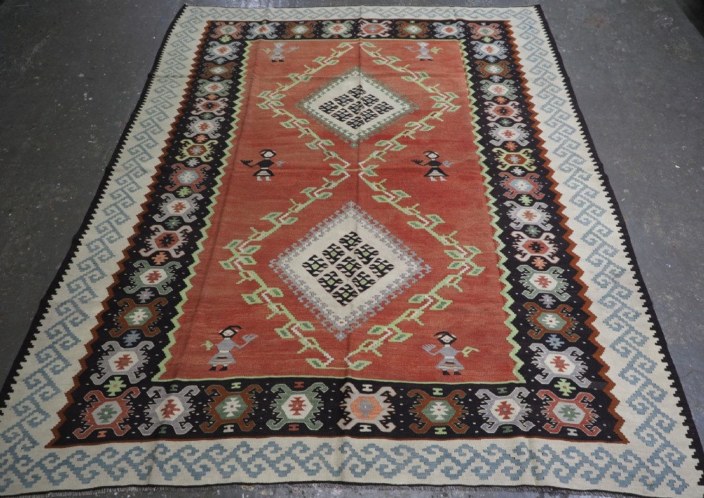 An antique woven wool Pirot Sarkoy kilim rug featuring a central terracotta red field decorated with diamond medallions and intricate geometric borders.