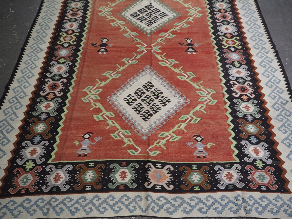 An antique woven wool Pirot Sarkoy kilim rug featuring a central terracotta red field decorated with diamond medallions and intricate geometric borders. View V