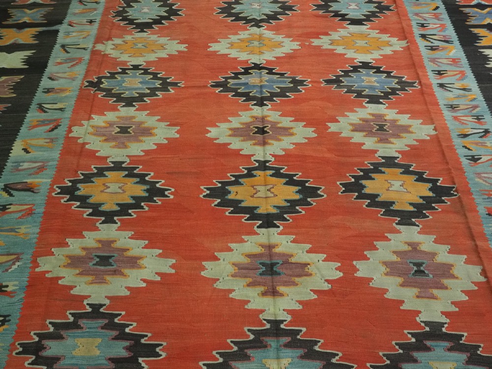 A large antique Pirot Sarkoy flat-weave wool kilim carpet featuring repeating diamond medallions on a terracotta field with dark geometric borders. View IV