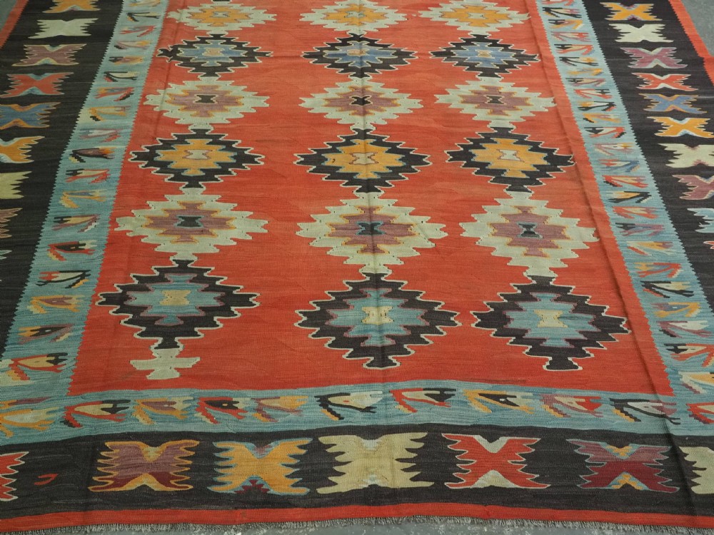 A large antique Pirot Sarkoy flat-weave wool kilim carpet featuring repeating diamond medallions on a terracotta field with dark geometric borders. View V